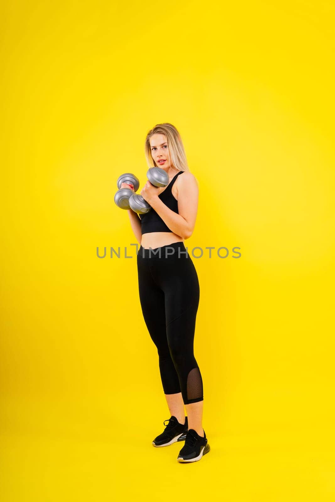 Perfect sporty female working out with dumbbells. Photo of woman in sportswear, studio shot