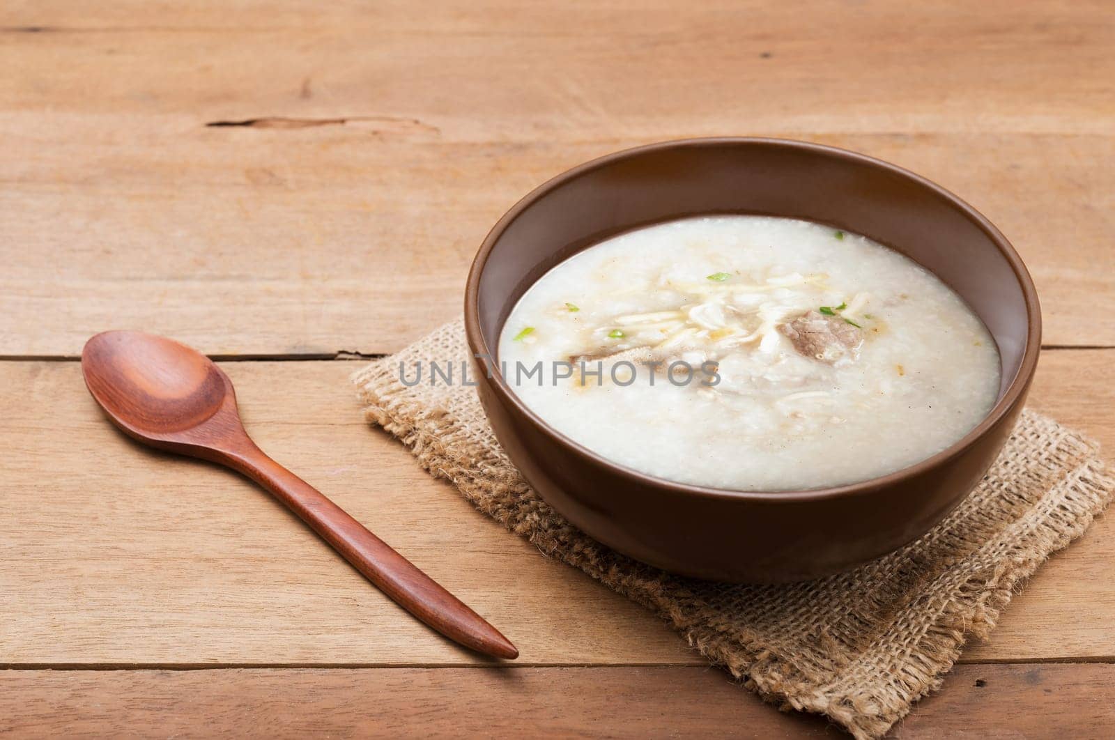 Traditional chinese porridge rice gruel in brown bowl with wooden spoon on wood table