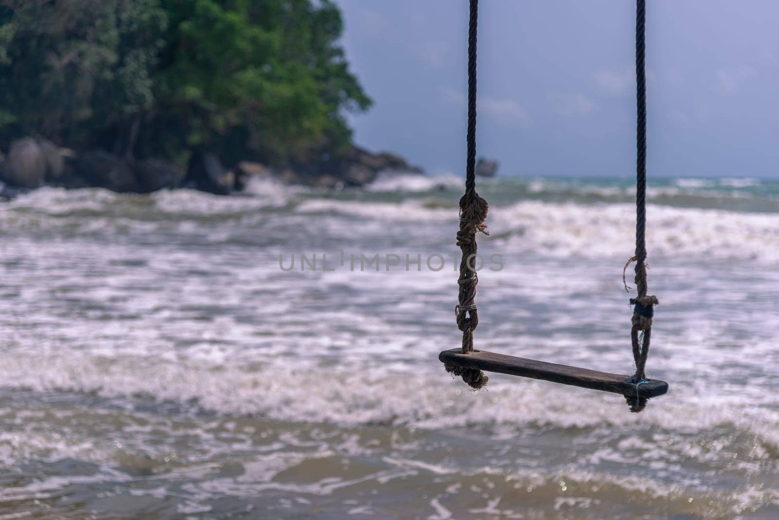 Swing hammock hanging under a tree on a beach with white sand and blue sky and emerald waters.