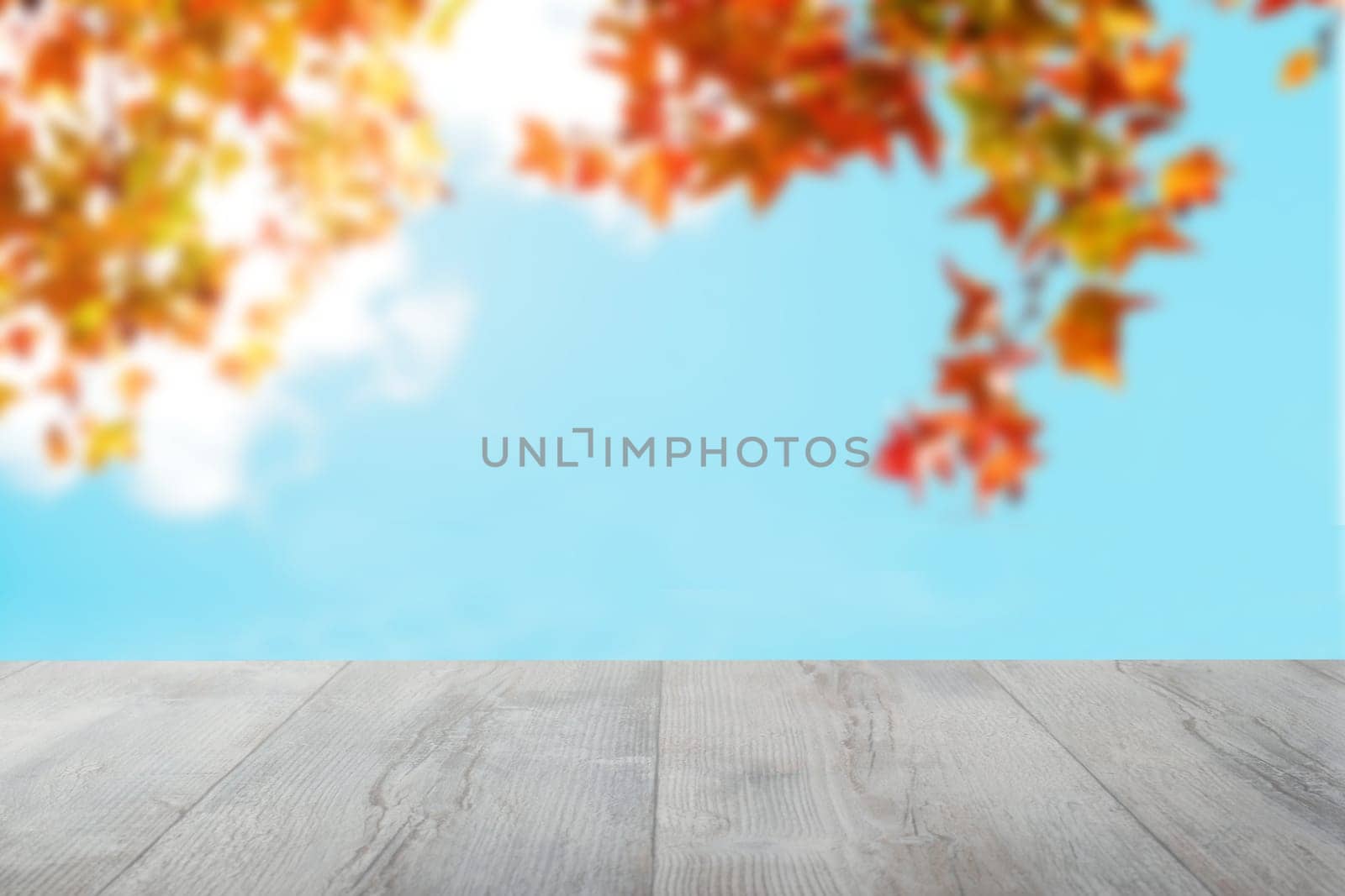 Empty wooden desk table over abstract blurred light blue sky and colorful autumn background with leaves. Template for your food and product display montage.