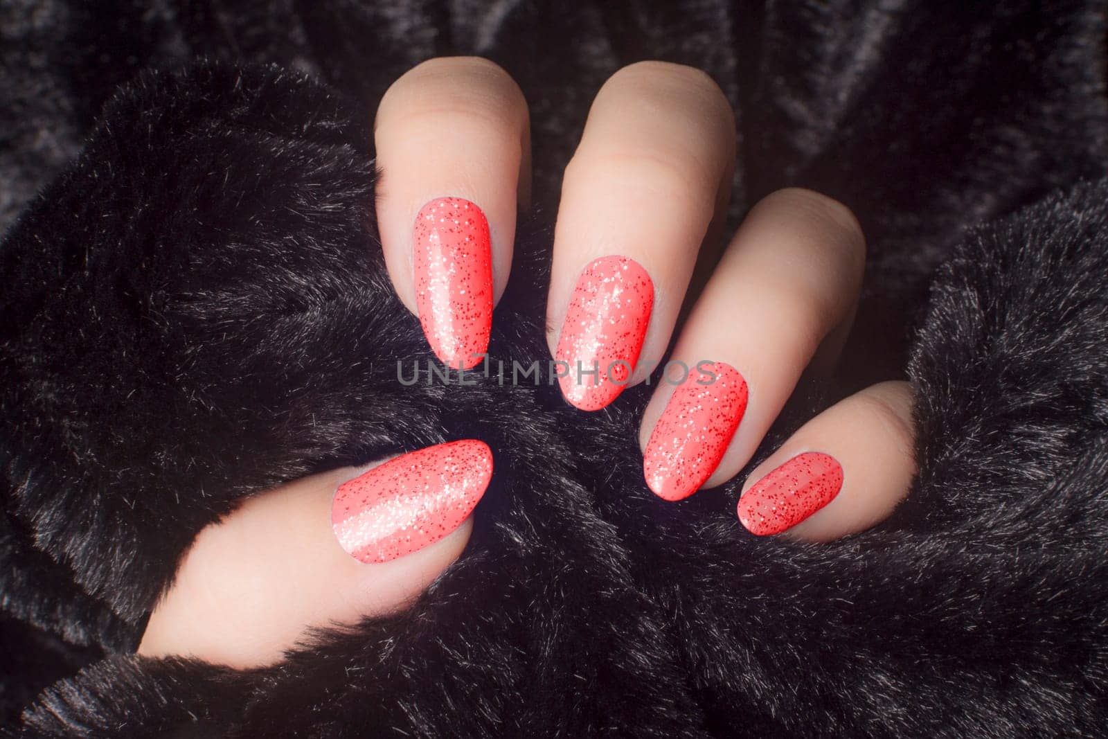 Female hand with glittered red nails is holding black fur, manicure and nail care concept.
