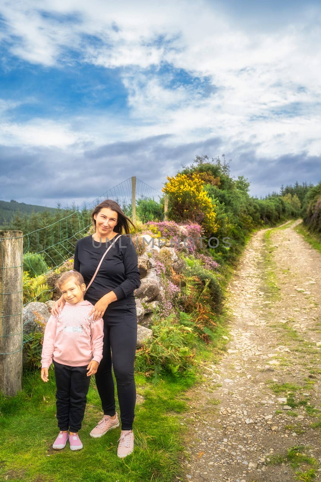 Mother and daughter standing on country road with colourful heathers and bushes in background. Family hiking in Lough Dan, Wicklow Mountains, Ireland