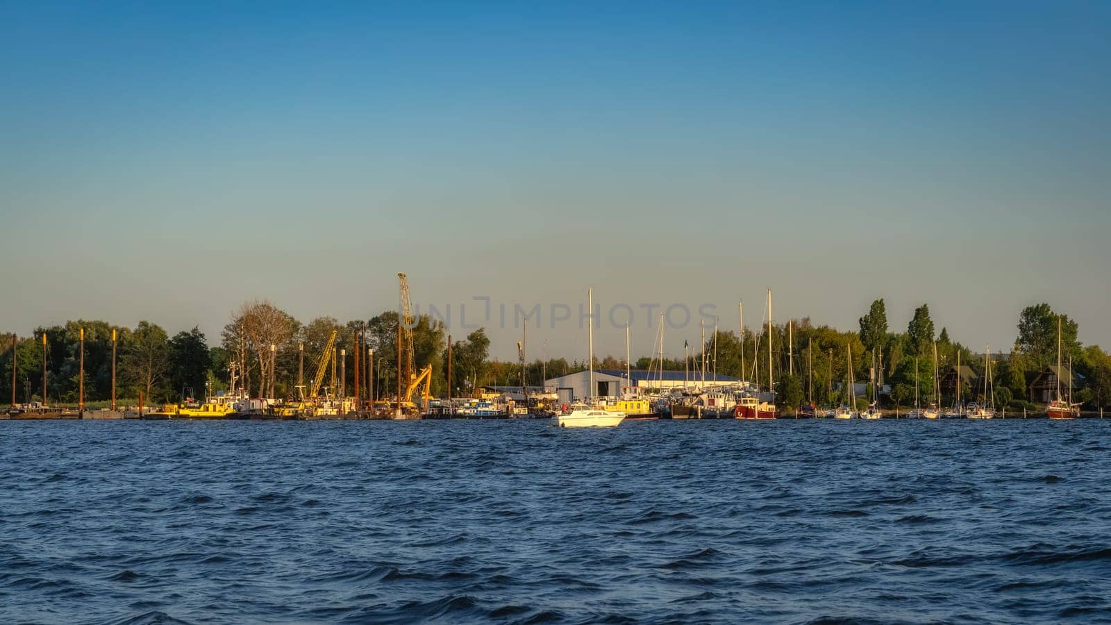 Shipyard and harbour of Szczecin Dabie marina with moored yachts and boats at sunset. Cranes and hangars in background, Poland
