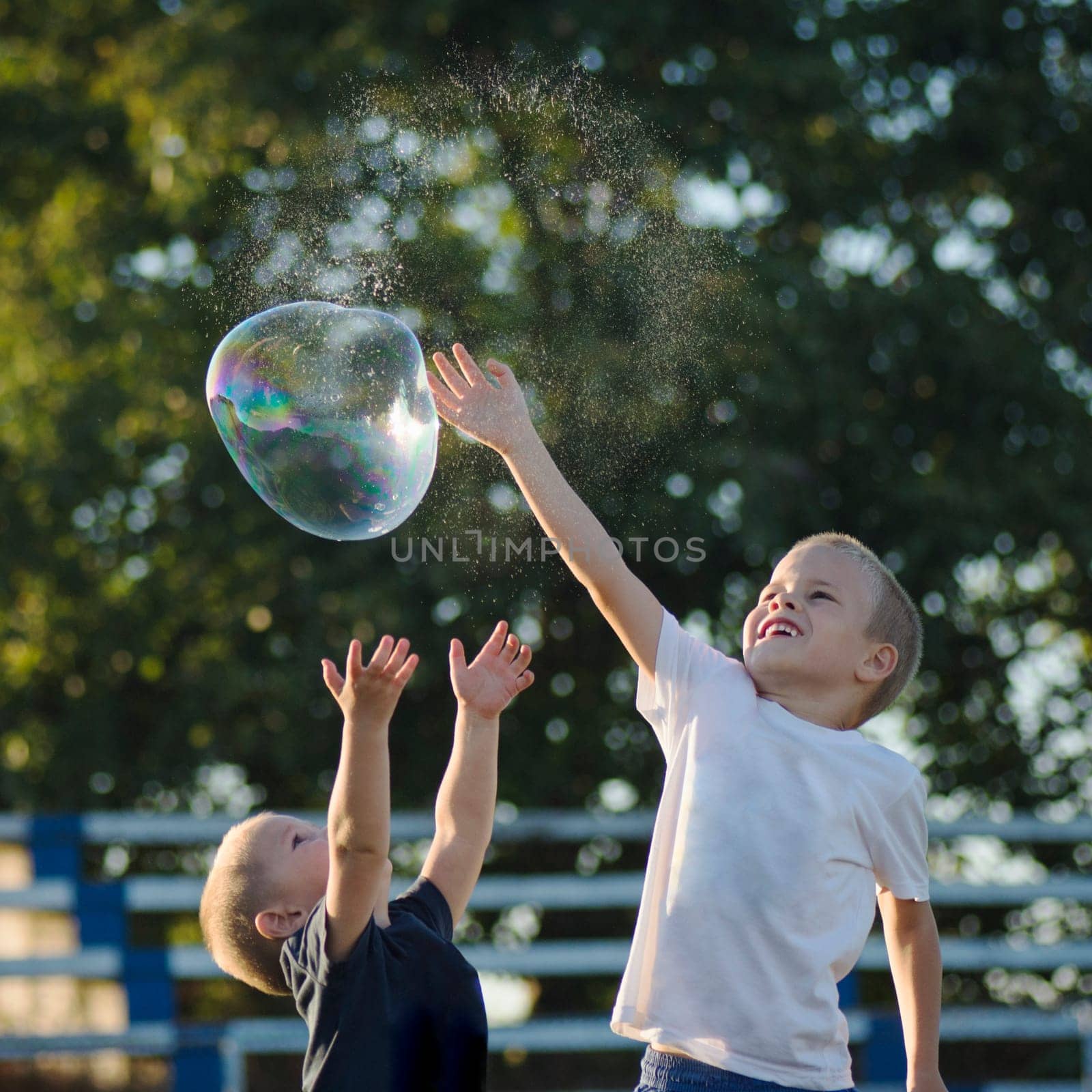 Two little boys are playing with soap bubble outdoors, happy and carefree childhood.