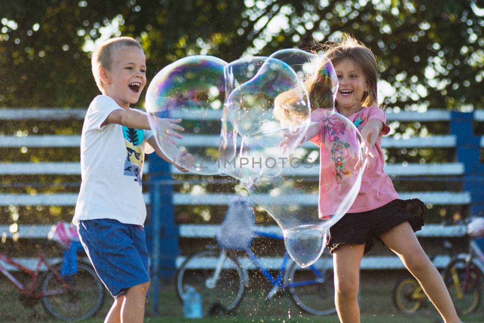 Happy children are playing with giant soap bubbles outdoors, joyful childhood concept.