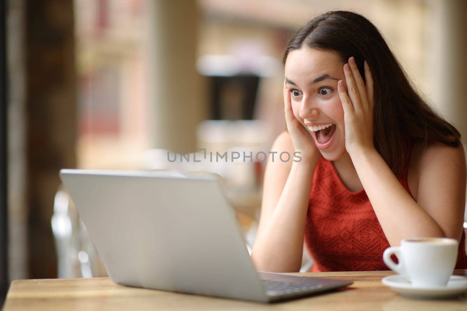Amazed woman finding good news on laptop sitting in a bar terrace