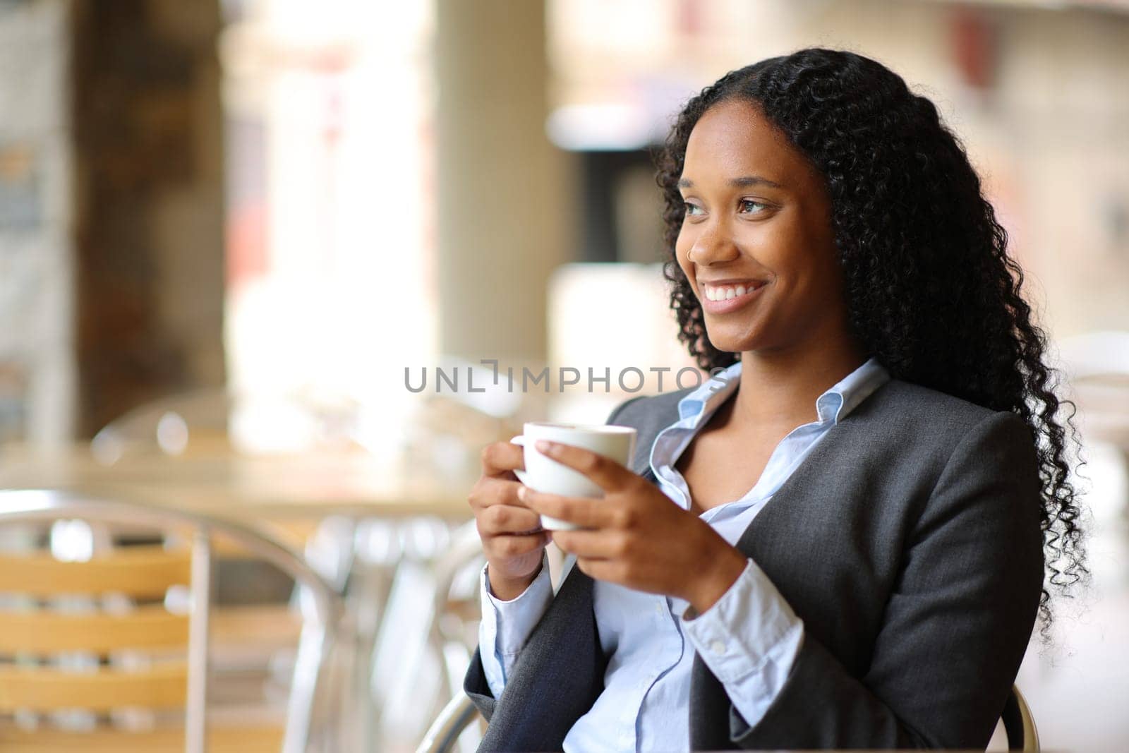 Happy black businesswoman enjoying coffee sitting in a restaurant terrace