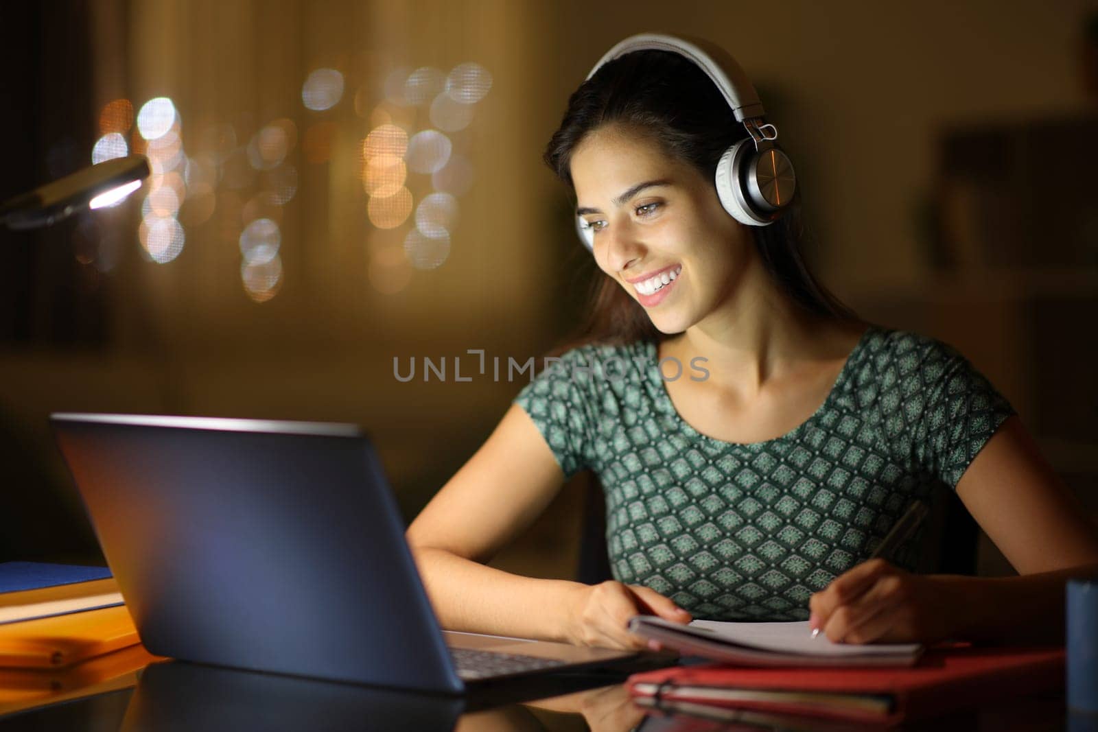 Happy student in the night elearning with laptop and headphone at home