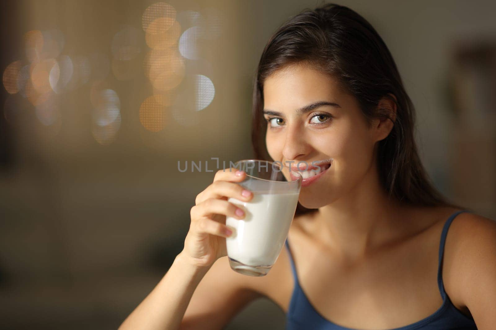 Happy woman drinking milk looking at camera in the night at home