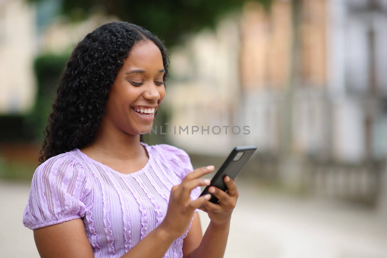 Happy black woman using smartphone walking in the street