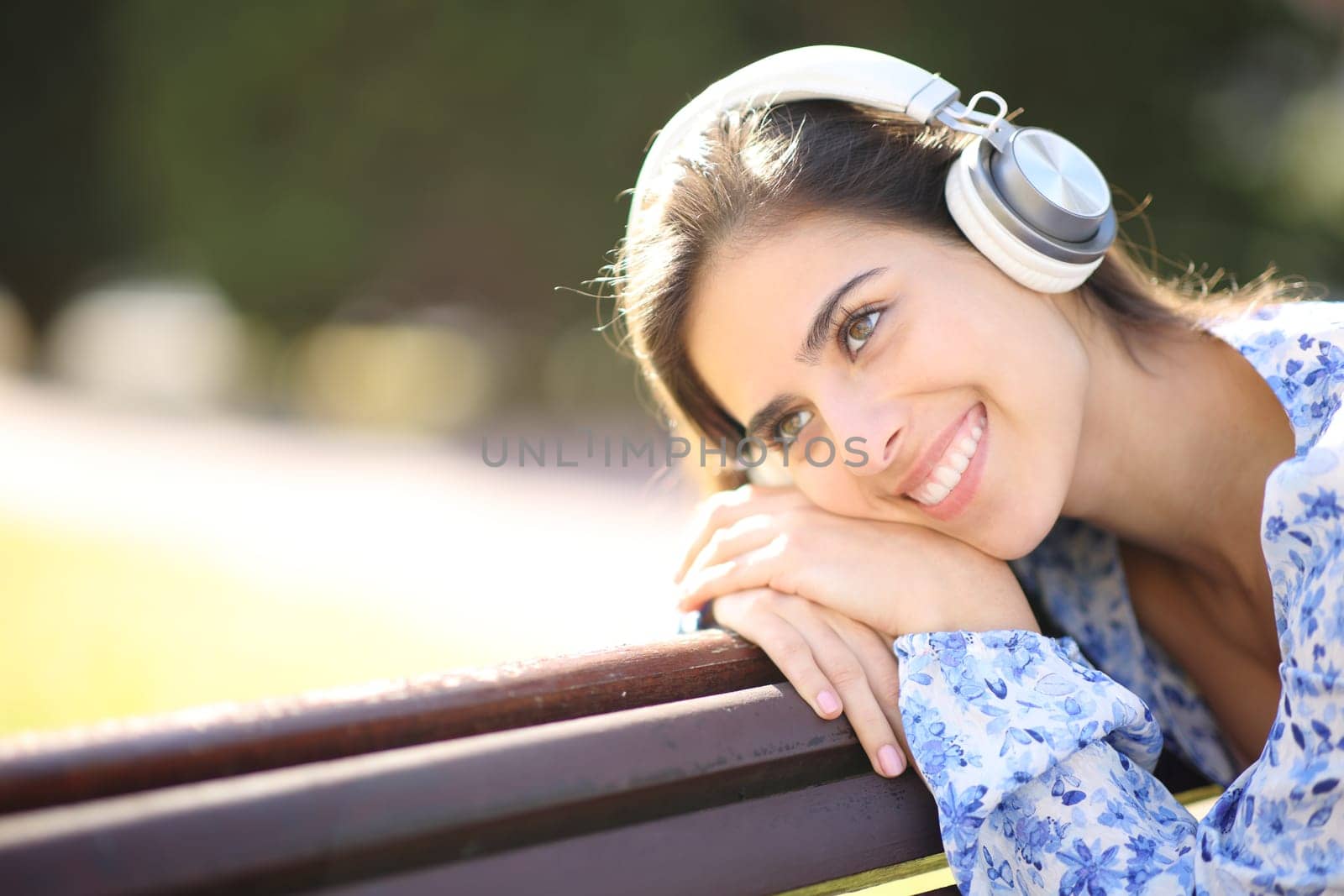 Happy woman wering headphone enjoying audio on a bench in a park