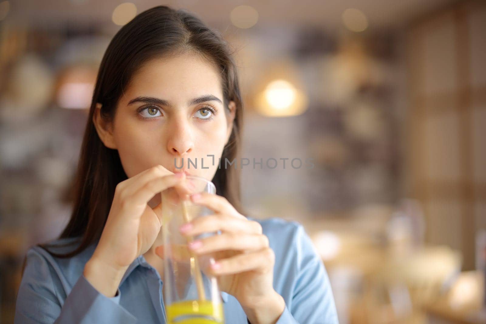 Front view of a distracted woman sipping orange juice with straw in a restaurant
