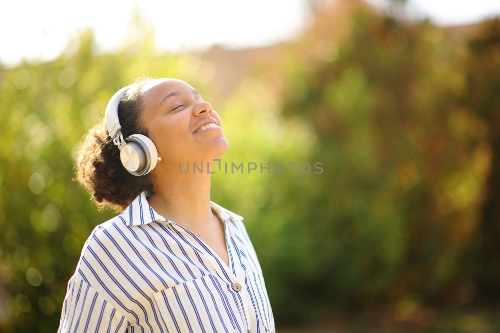 Happy black woman meditating listening audio guide with headphone in a park