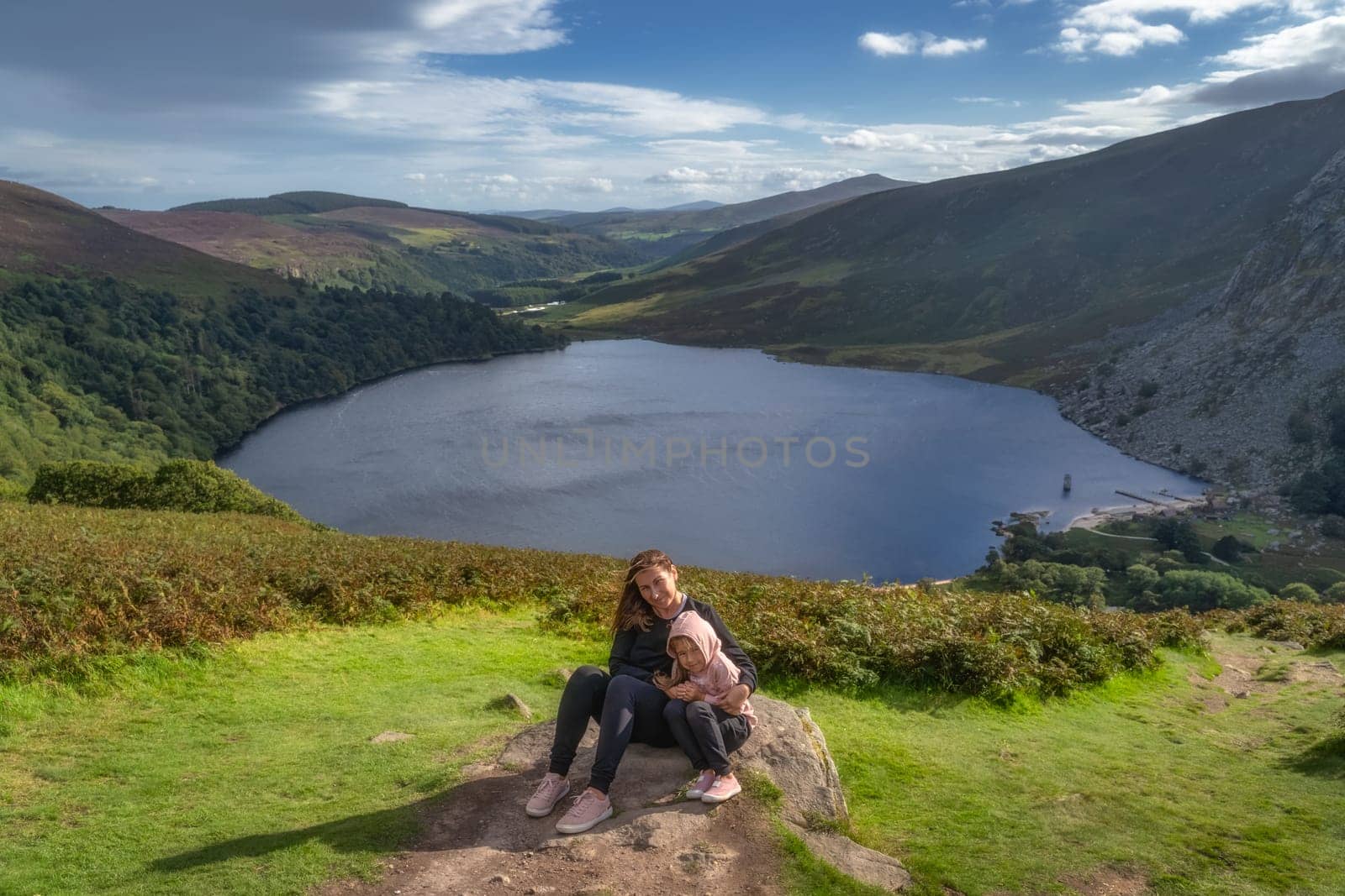 Mother and daughter, family, sitting on a large rock and smiling. Lough Tay, called Guiness Lake in Wicklow Mountains, Ireland
