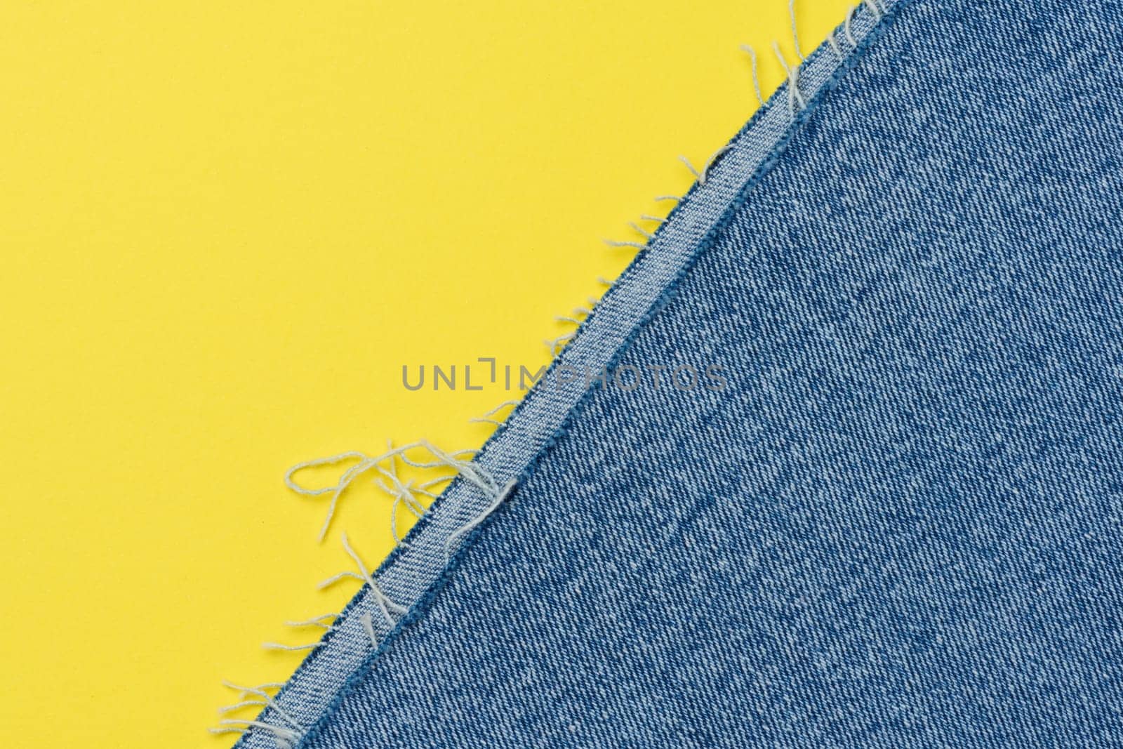 Torn edges of blue jeans on a yellow background