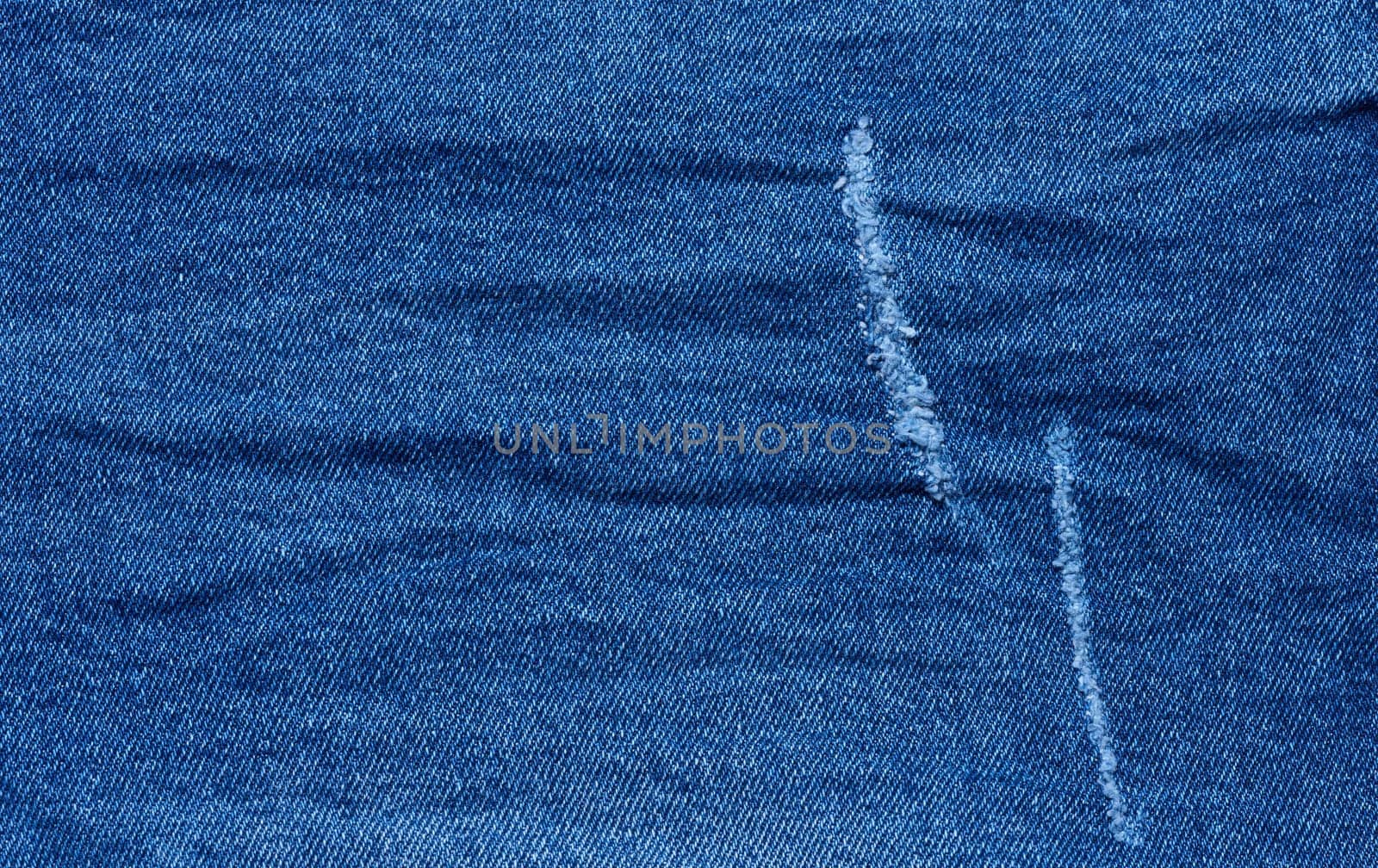Fragment of blue jeans fabric with a hole, full frame, close up