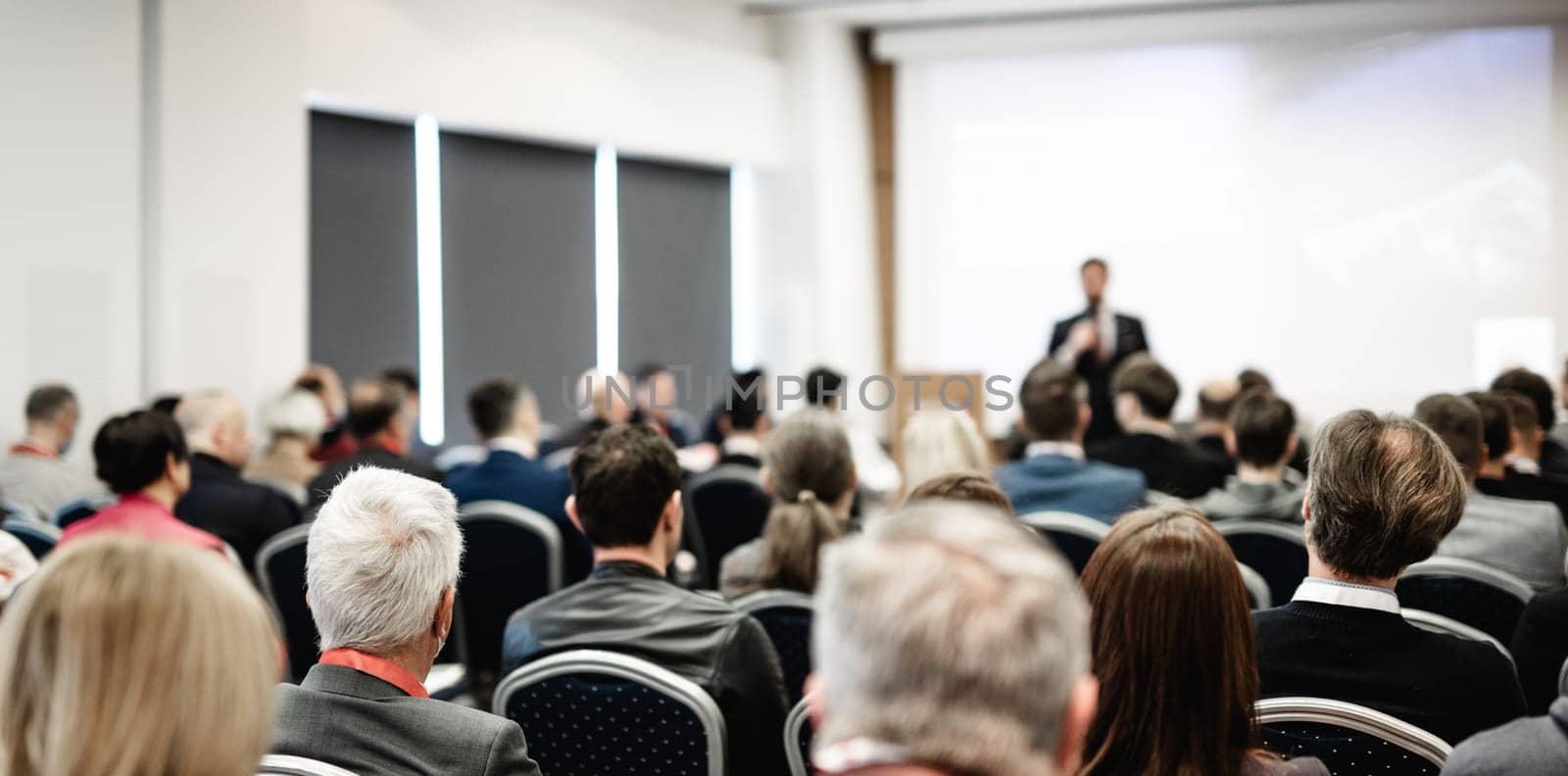 Speaker giving a talk in conference hall at business event. Rear view of unrecognizable people in audience at the conference hall. Business and entrepreneurship concept