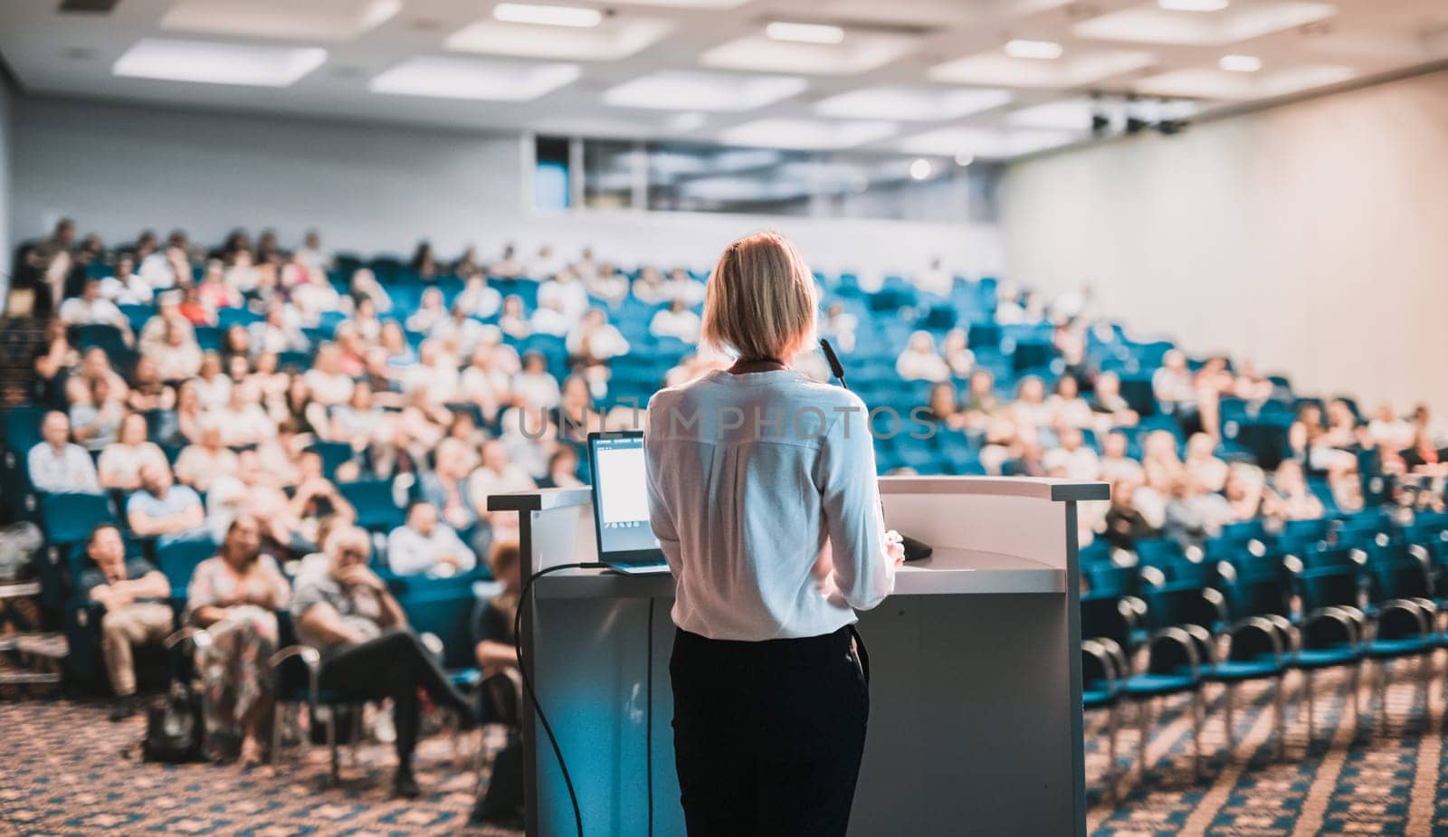Female speaker giving a talk on corporate business conference. Unrecognizable people in audience at conference hall. Business and Entrepreneurship event