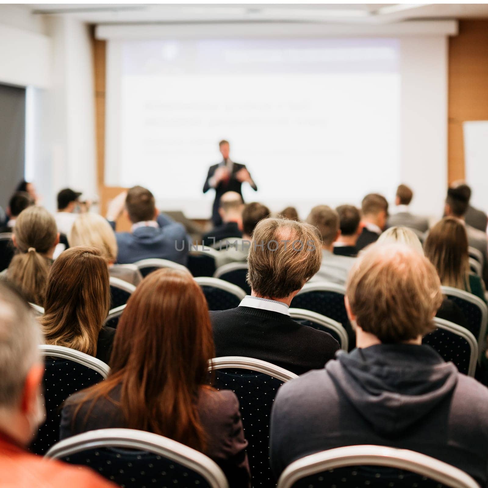 Speaker giving a talk in conference hall at business event. Rear view of unrecognizable people in audience at the conference hall. Business and entrepreneurship concept