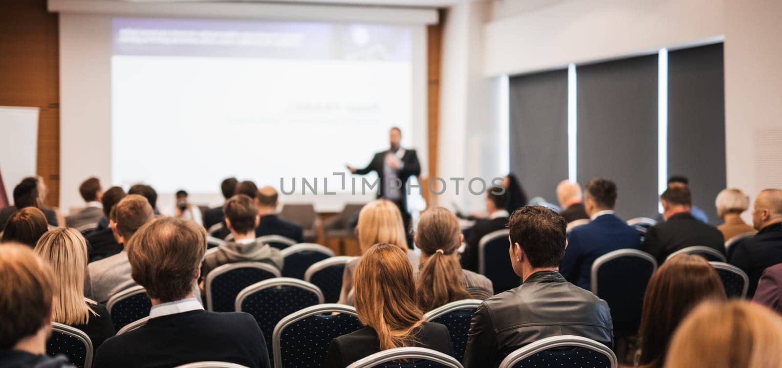 Speaker giving a talk in conference hall at business event. Rear view of unrecognizable people in audience at the conference hall. Business and entrepreneurship concept