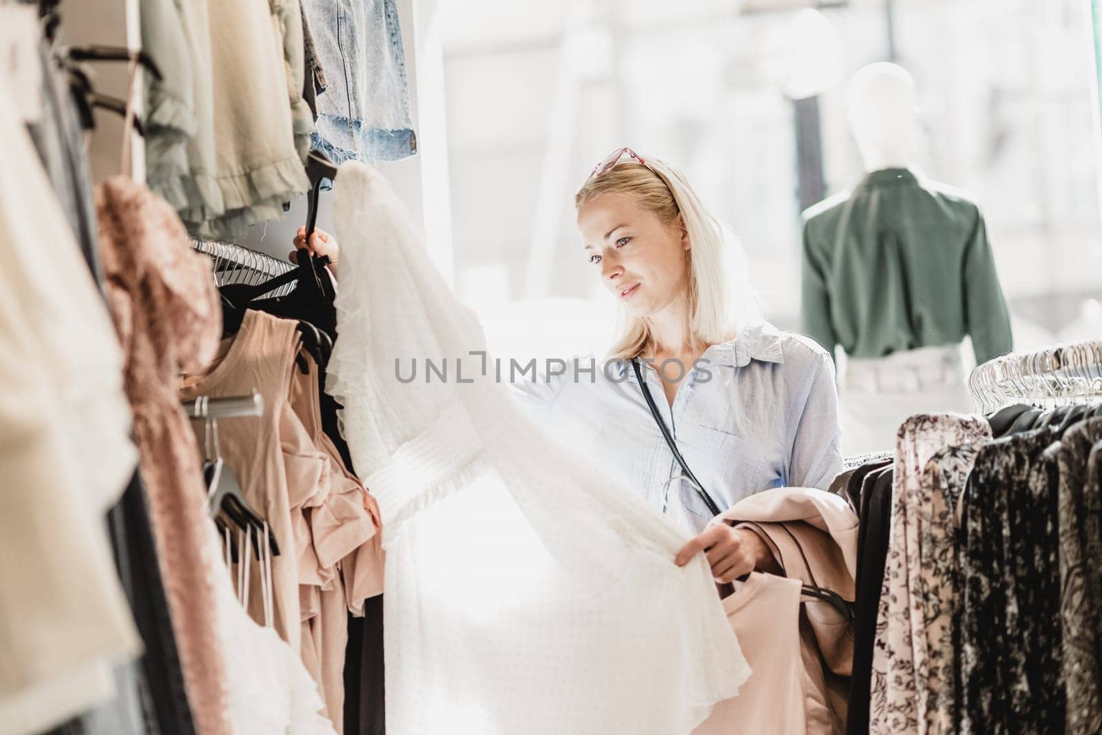Woman shopping clothes. Female shopper looking at fashionable clothes indoors in clothing store.