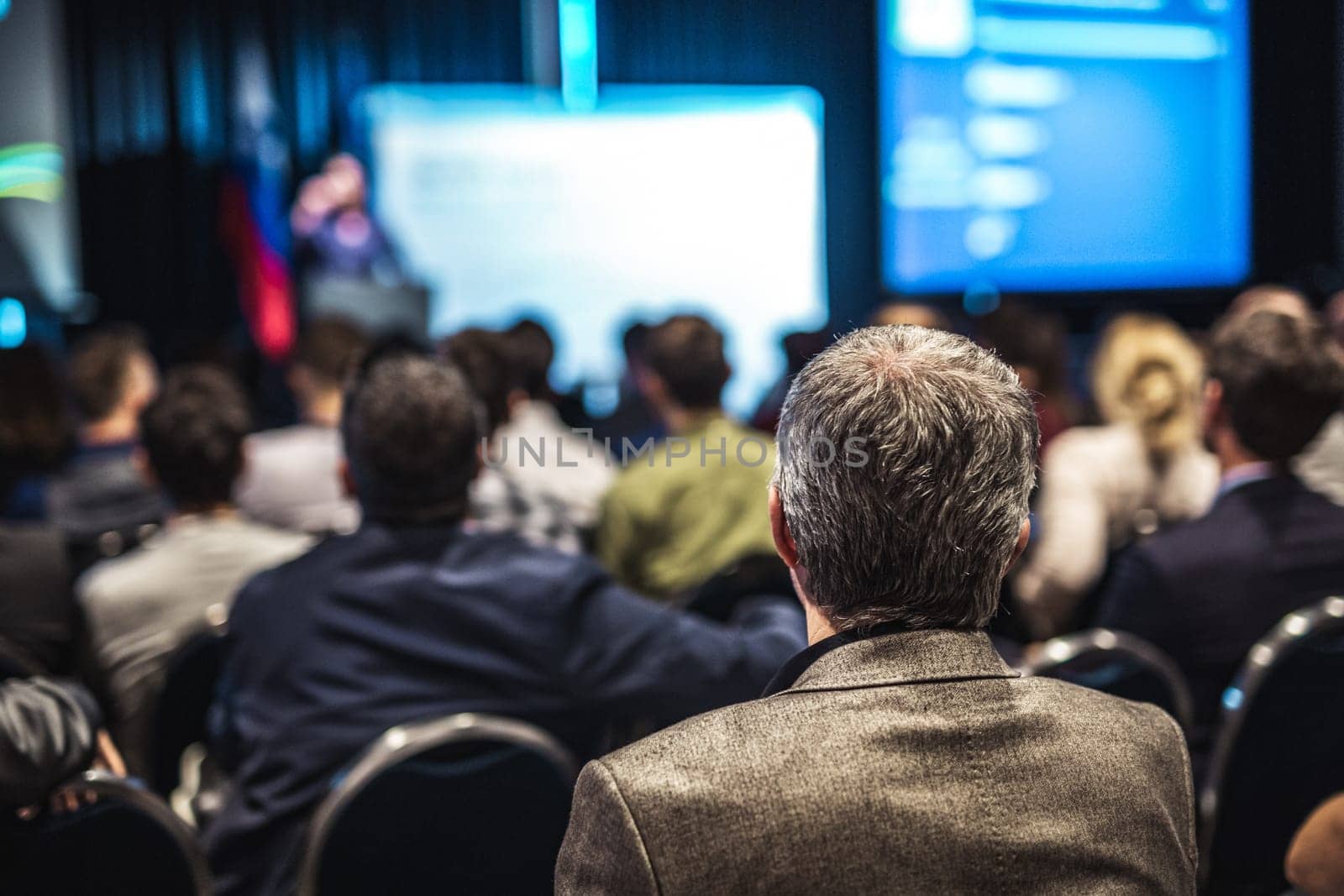 Speaker giving a talk in conference hall at business event. Rear view of unrecognizable people in audience at the conference hall. Business and entrepreneurship concept
