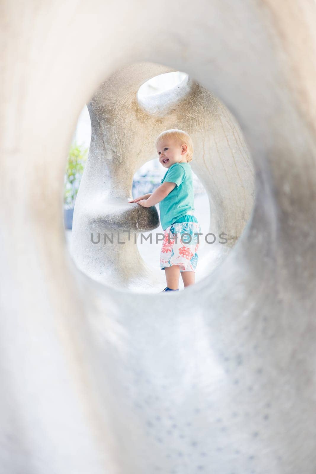Child playing on outdoor playground. Toddler plays on school or kindergarten yard. Active kid on stone sculpured slide. Healthy summer activity for children. Little boy climbing outdoors