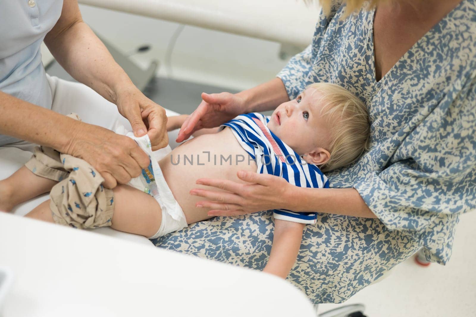 Infant baby boy child being examined by his pediatrician doctor during a standard medical checkup in presence and comfort of his mother. National public health and childs care care koncept