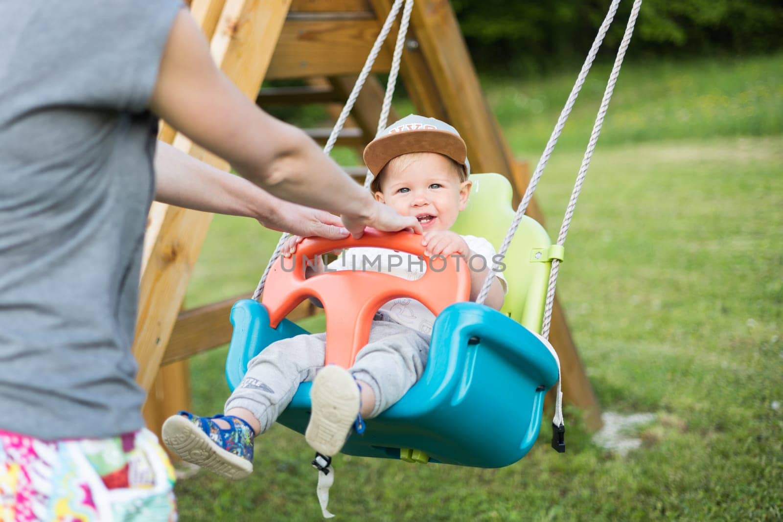 Mother pushing her infant baby boy child on a swing on playground outdoors