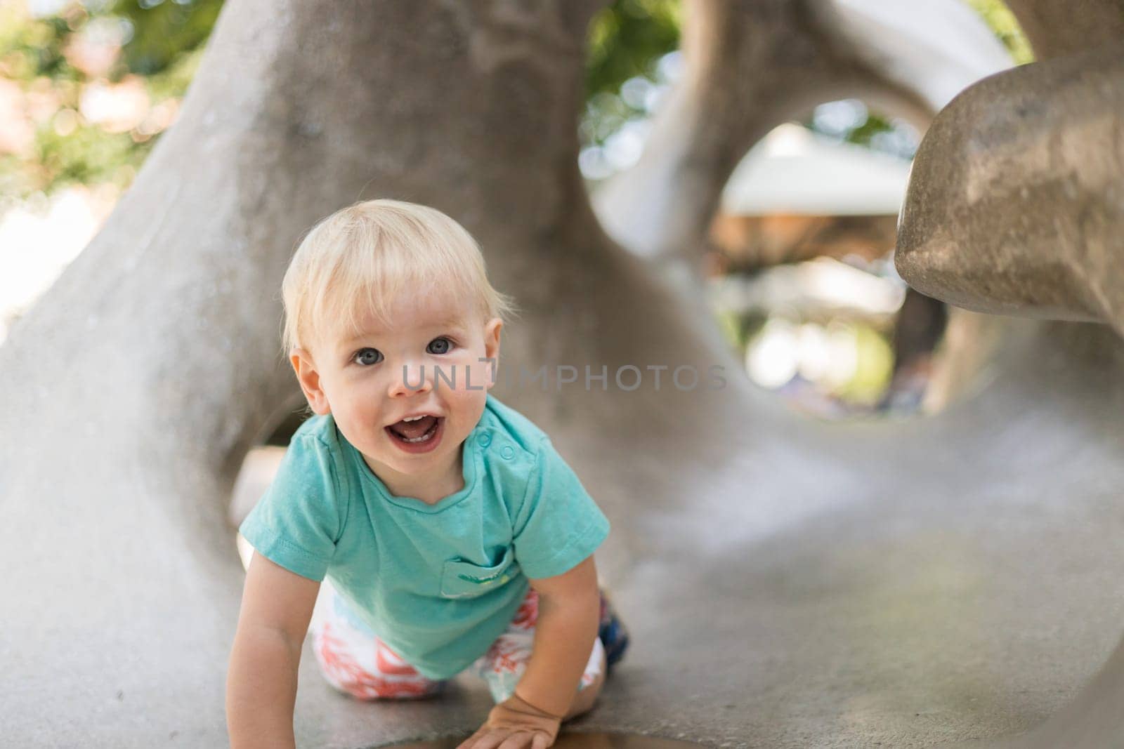 Child playing on outdoor playground. Toddler plays on school or kindergarten yard. Active kid on stone sculpured slide. Healthy summer activity for children. Little boy climbing outdoors