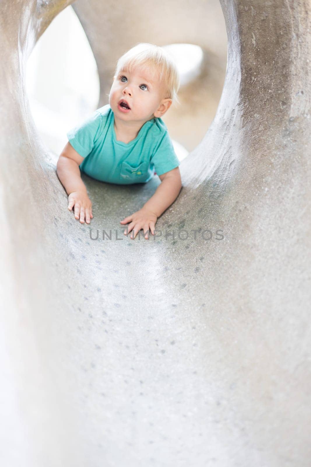 Child playing on outdoor playground. Toddler plays on school or kindergarten yard. Active kid on stone sculpured slide. Healthy summer activity for children. Little boy climbing outdoors