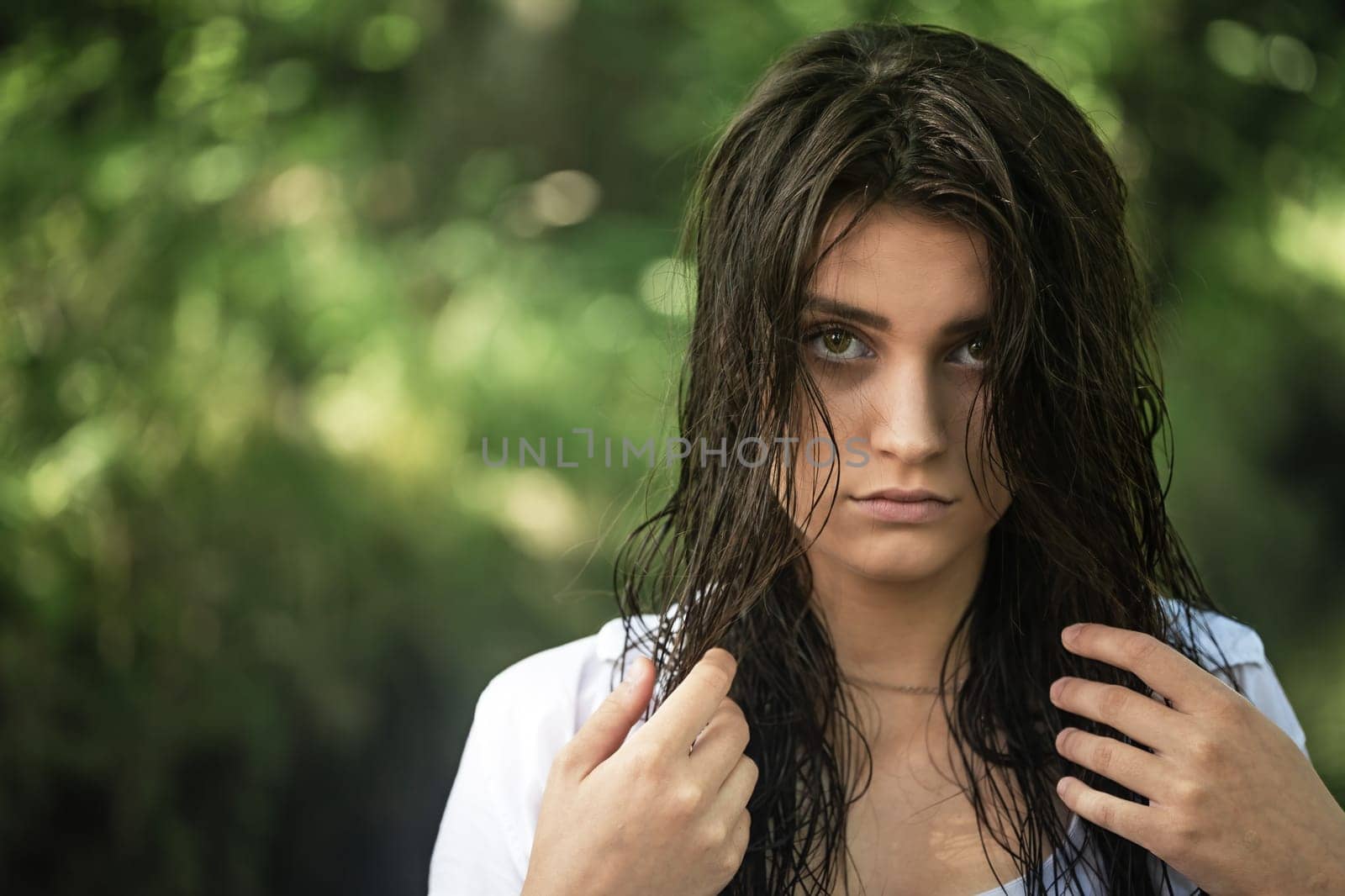 Sad attractive girl is holding her wet hair with both hands looking at the camera closeup. Horizontally.