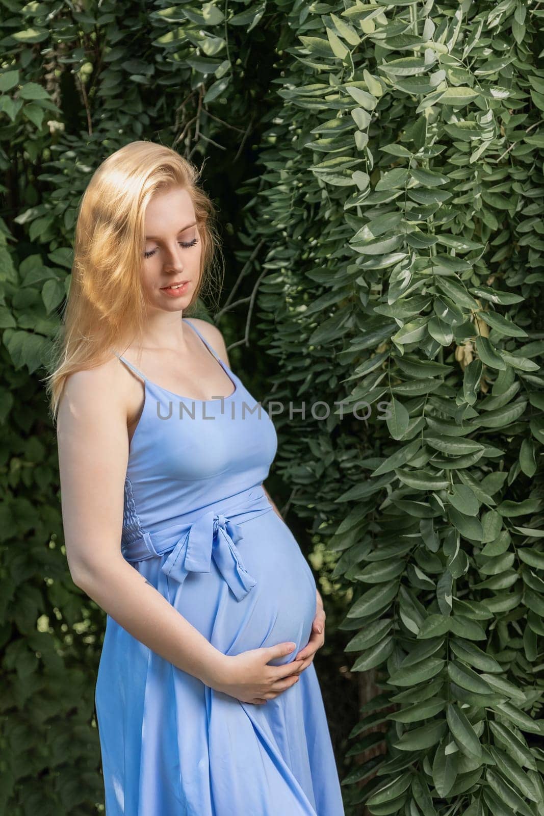 Pregnant beautiful young blonde woman is posing outdoors. Horizontally.