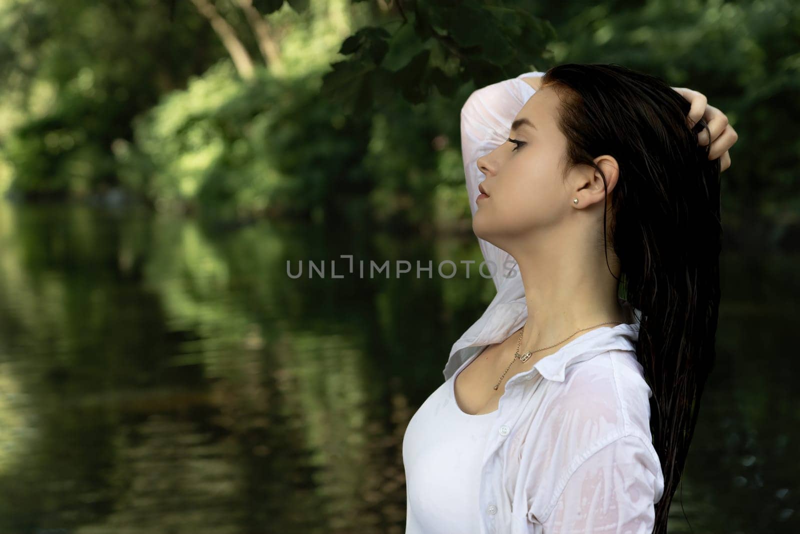 Side view portrait of beautiful brunette girl with wet hair posing in the river. Horizontally.