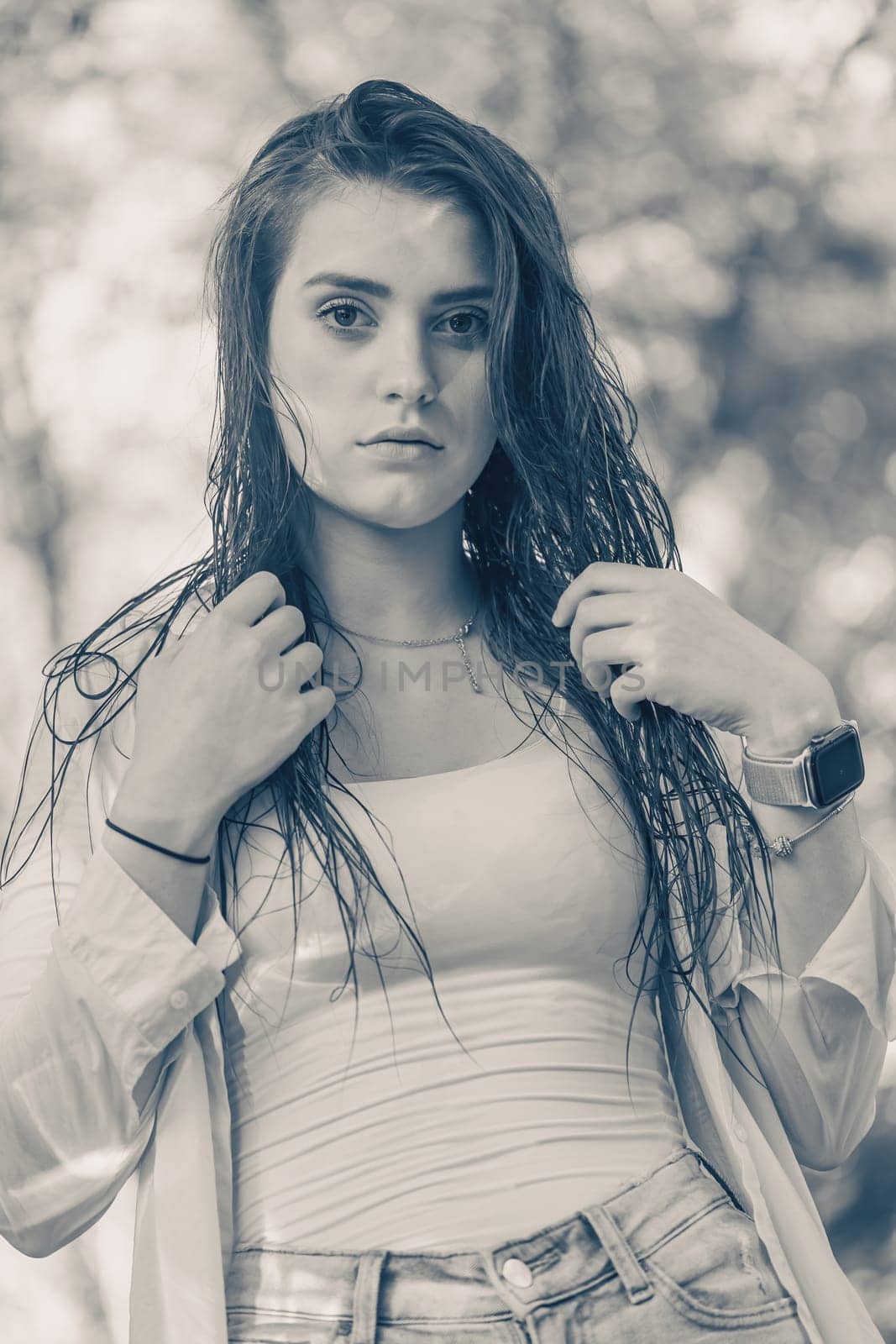 Monochrome photo in a blue hue shows beautiful brunette girl with wet hair posing outside.  Vertically.