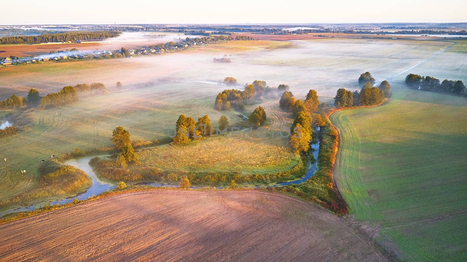 Warm sunny September morning. Autumn beautiful fog landscape. Small river curves in trees. Bright sunny misty riverside. Scenic view of rural sunrise. Village in Agriculture fields. Europe, Belarus