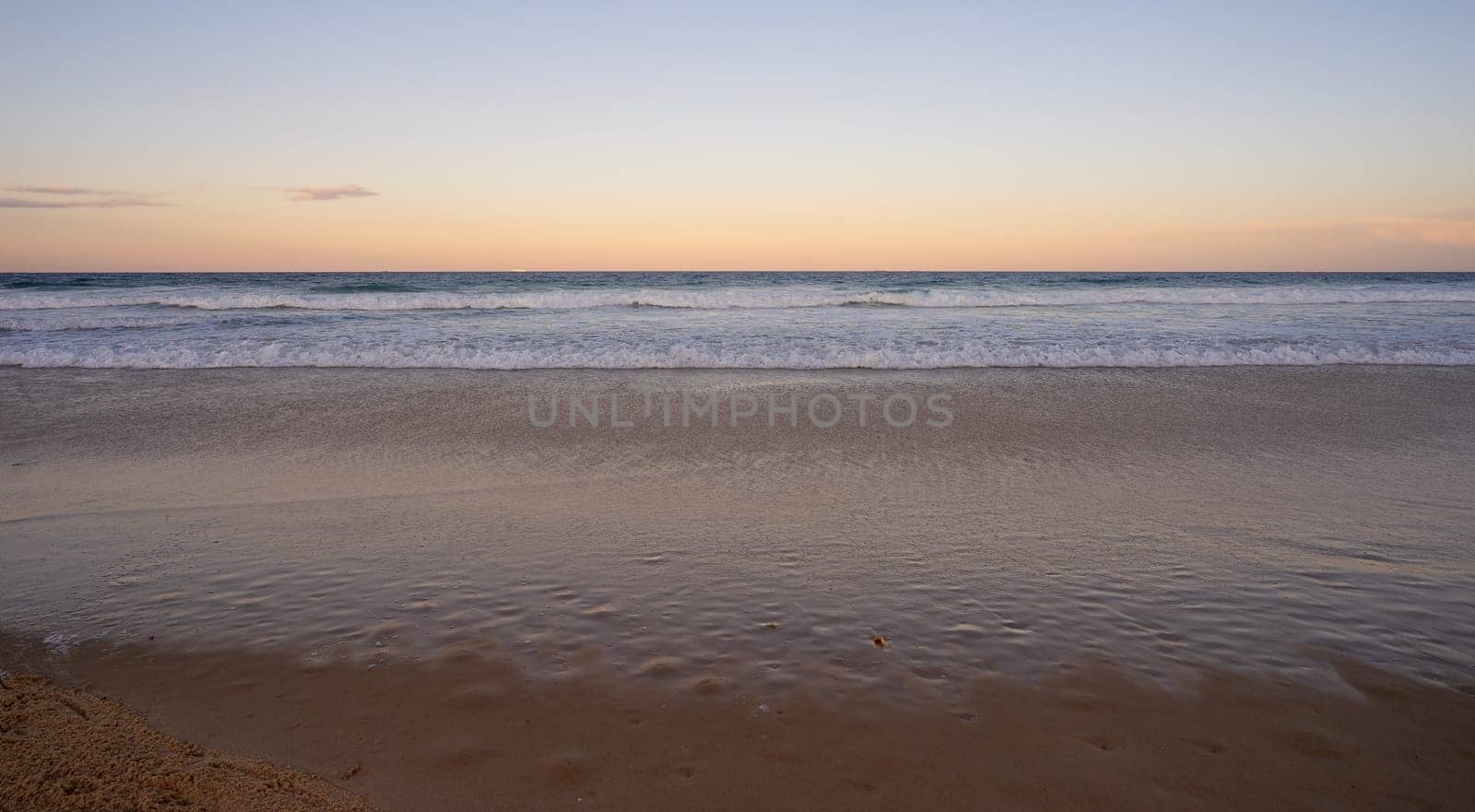 Looking east over the Pacific Ocean, Queensland, as the sun sets in the west, waiting for the full moon to rise above the horizon while the surf waves break on a sandy beach at Kawana, Sunshine Coast, a popular holiday destination.