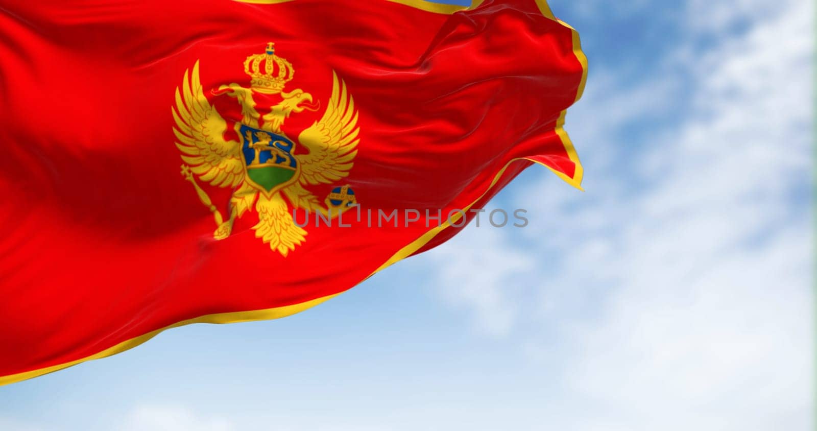 National flag of Montenegro waving in the wind on a clear day. Red with a golden border and features the national coat of arms in its center. 3d illustration render. Selective focus. Fluttering fabric
