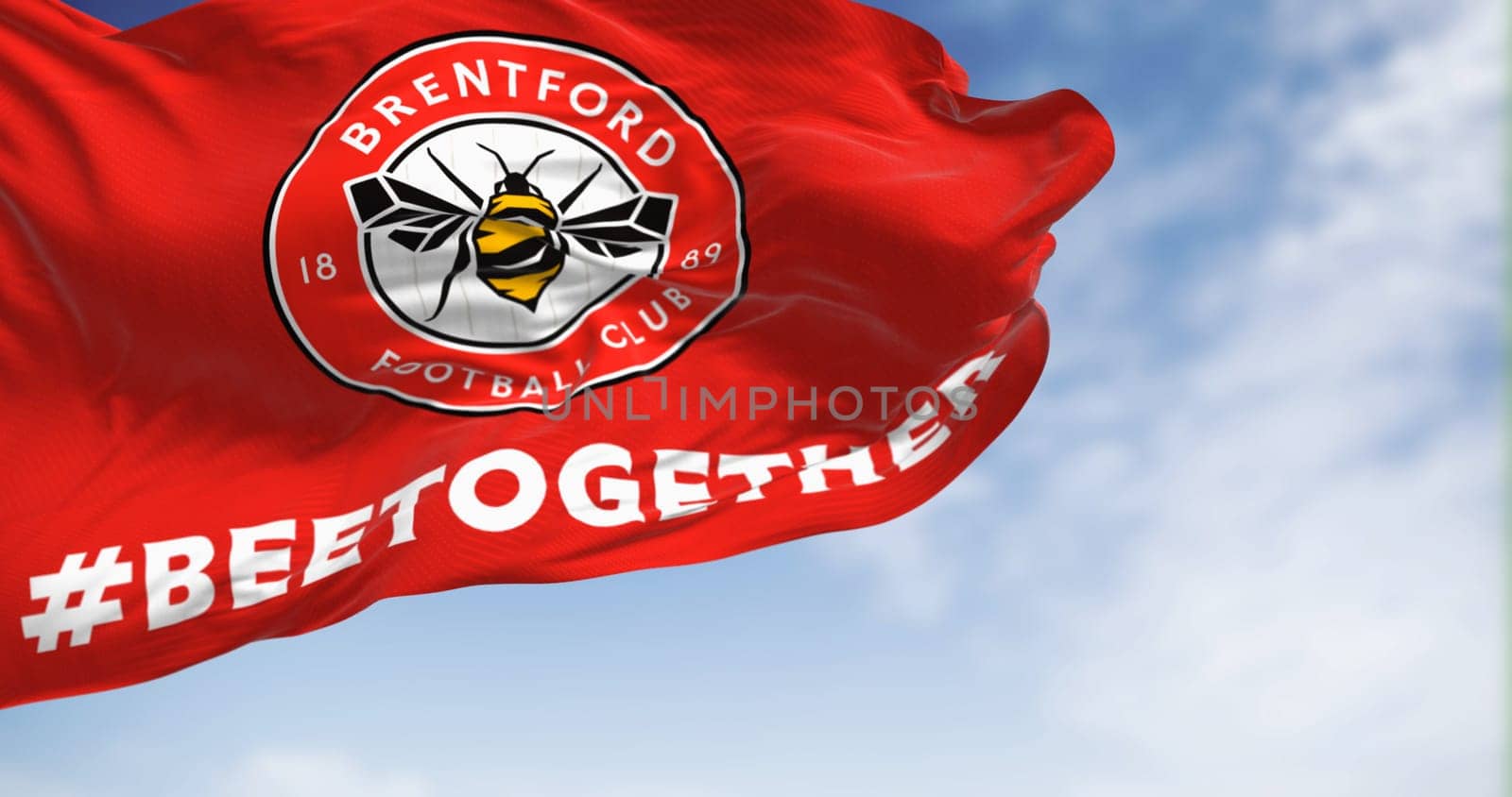 London, UK, Feb 19 2023: Brentford Football Club flag waving in the wind on a clear day. Circular emblem with a bee inside on red. Illustrative editorial 3d illustration render