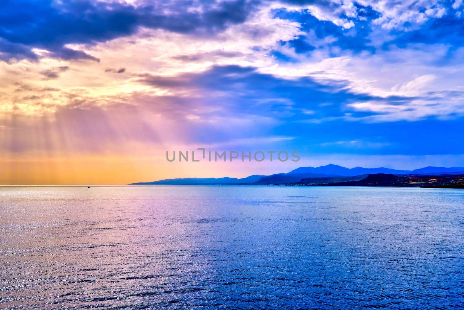 Colorful seascape with colorful clouds and bright sun rays cast over calm sea waters and hazy distant shores. Sunrise or sunset in Mediterranean sea, soft focus background.