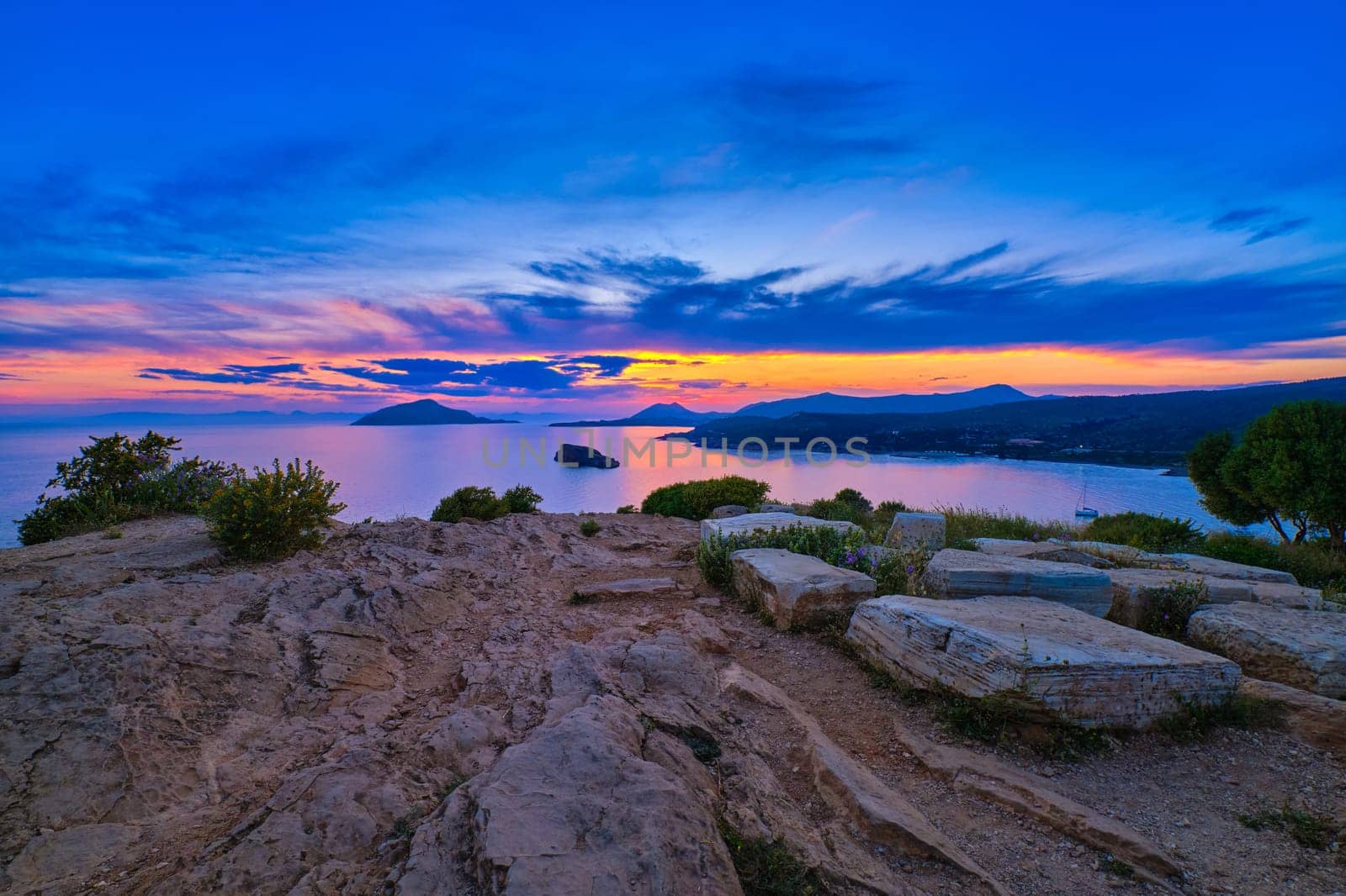 Sunset at ancient Temple of Poseidon, Sounio, Greece. Tranquil coastal landscape with clear blue waters.