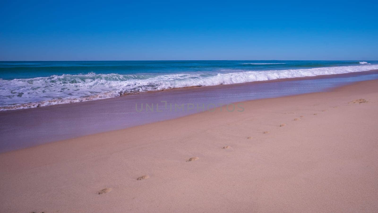 For a background with the ocean with clear blue sky, surf and breaking waves, along a wet sandy stretch of beach in an idyllic, romantic, relaxing holiday destination of Sunshine Coast, Queensland, Australia