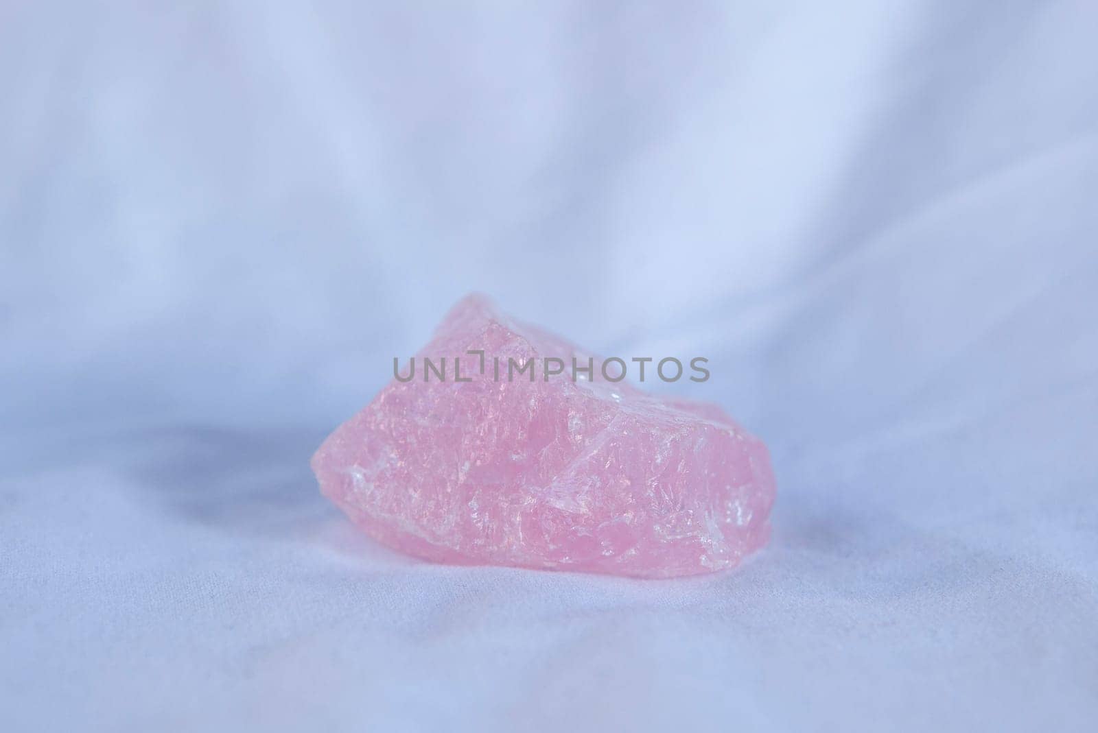 Rose quartz fragment, believed to have beneficial health properties. Isolated over white fabric cloth