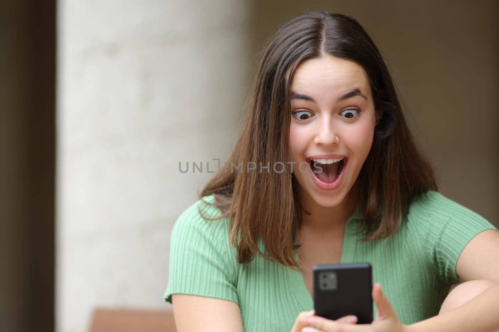 Front view portrait of an amazed woman checking surprising content on phone in the street