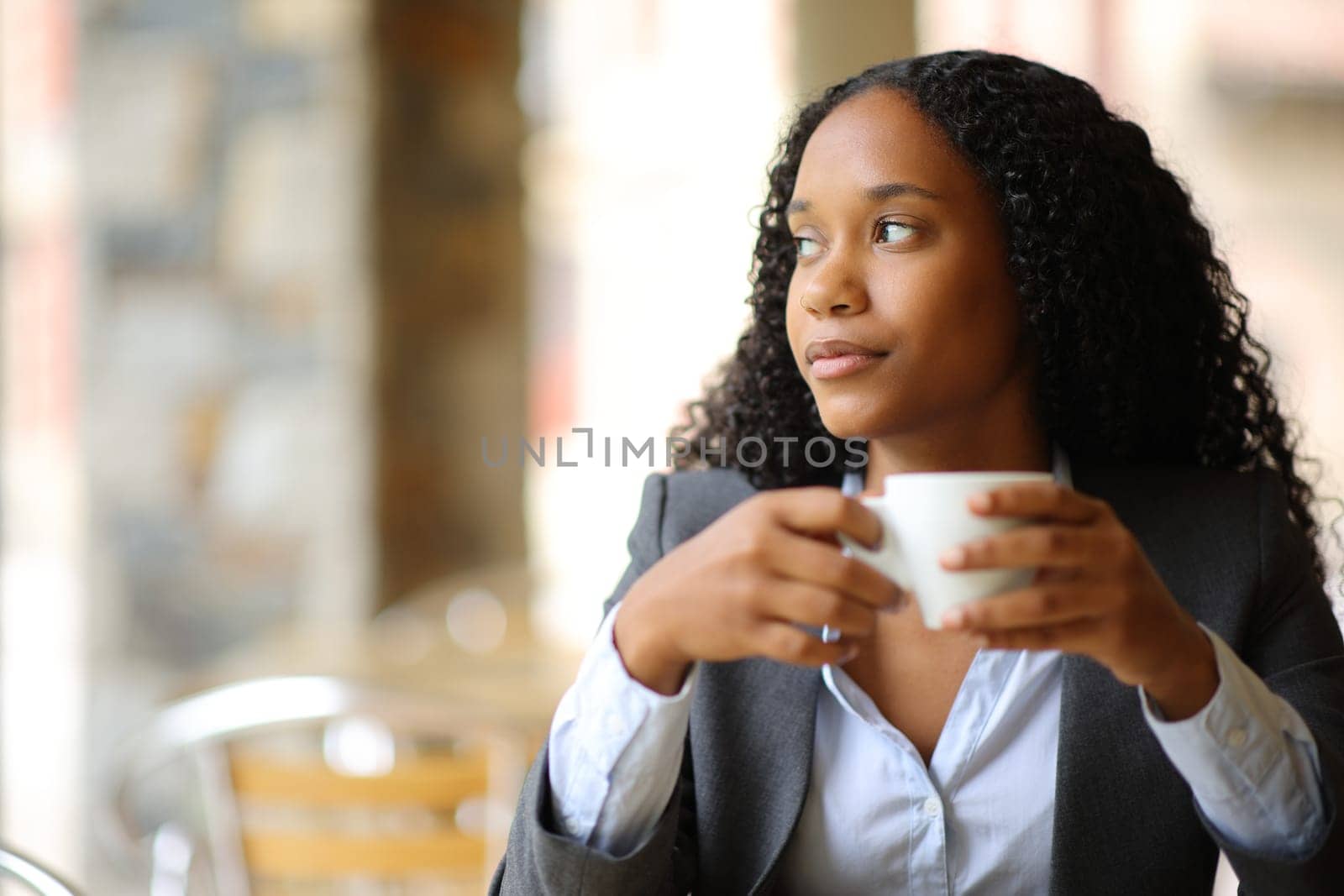 Black serious businesswoman drinking coffee at breakfast thinking looking at side in a restaurant terrace