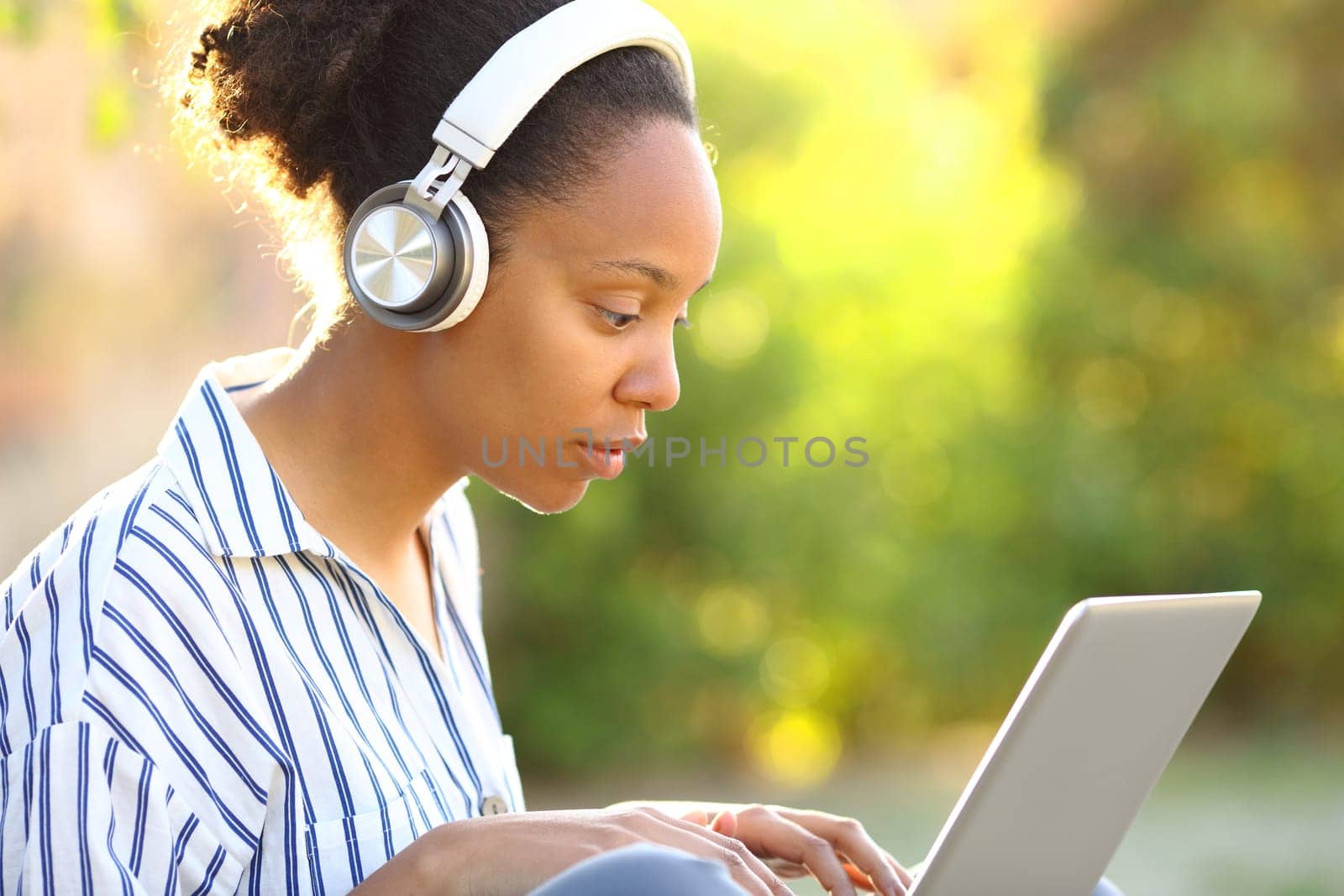 Black woman wearing headphone using laptop in a park