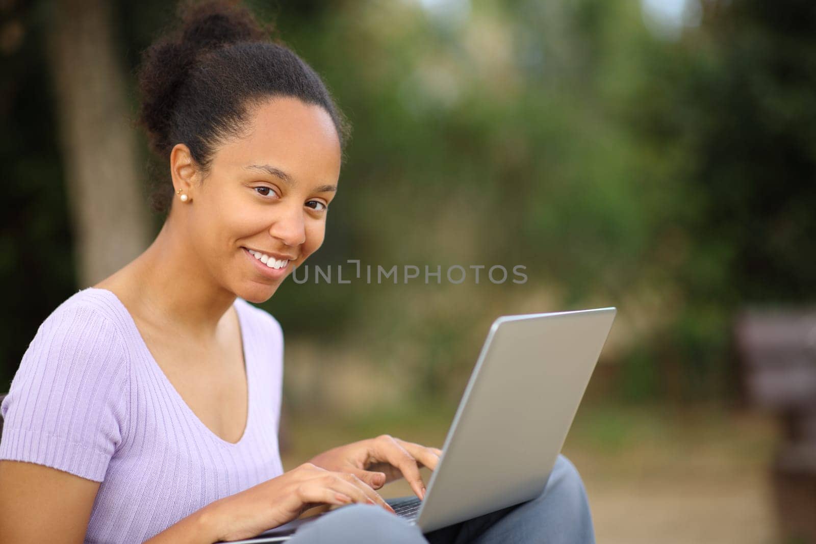 Black woman looks at you using laptop sitting in a park