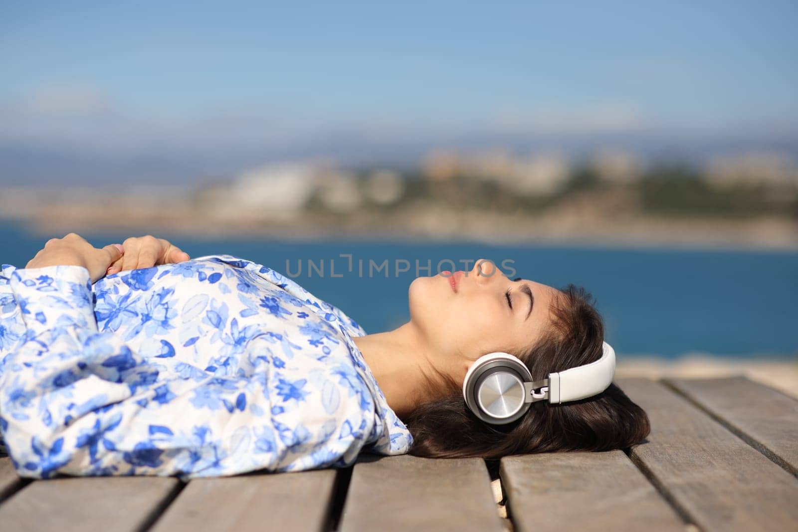 Side view portrait of a relaxed woman wearing headphone listening audio lying in the coast