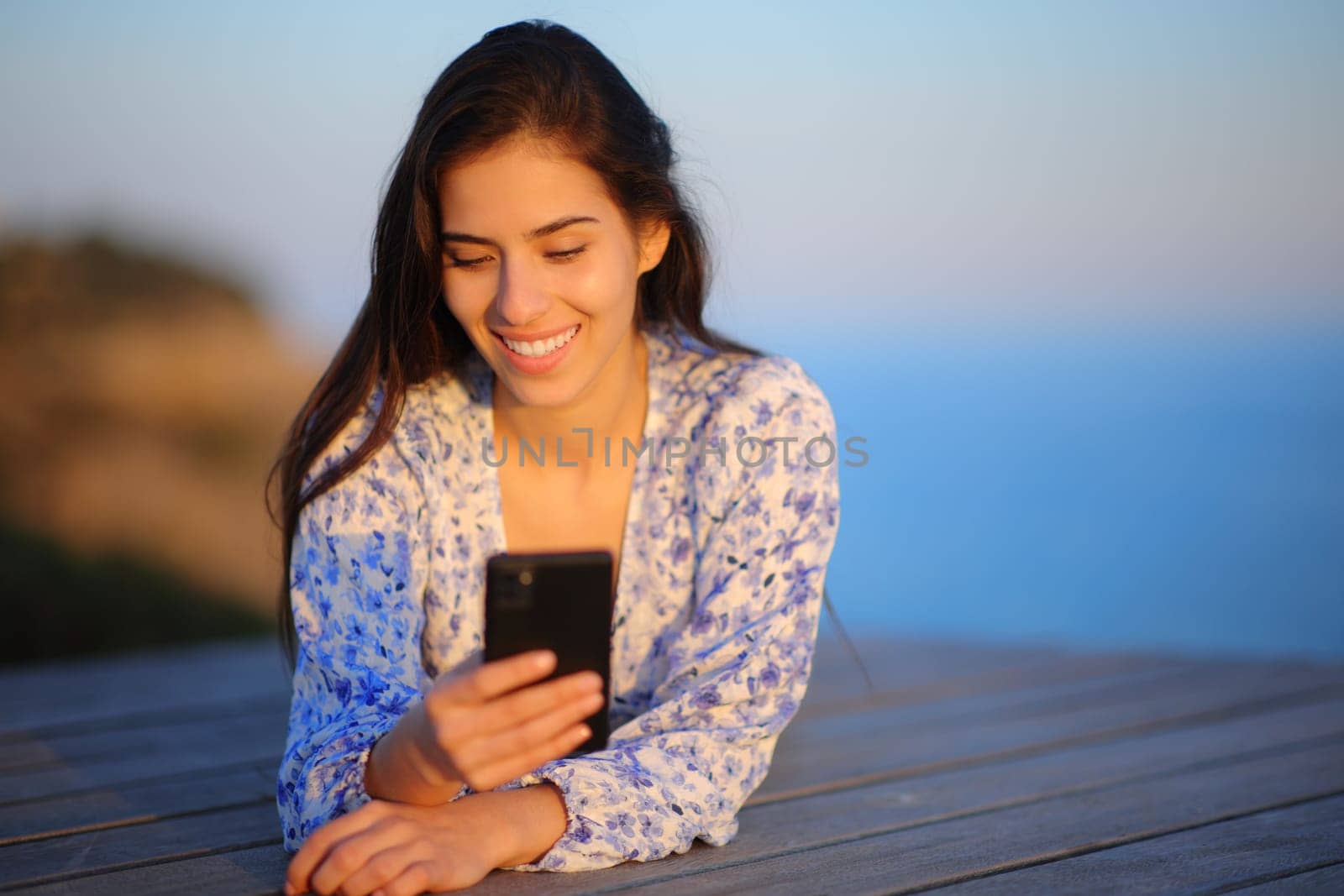 Front view portrait of a happy woman using smart phone in the coast