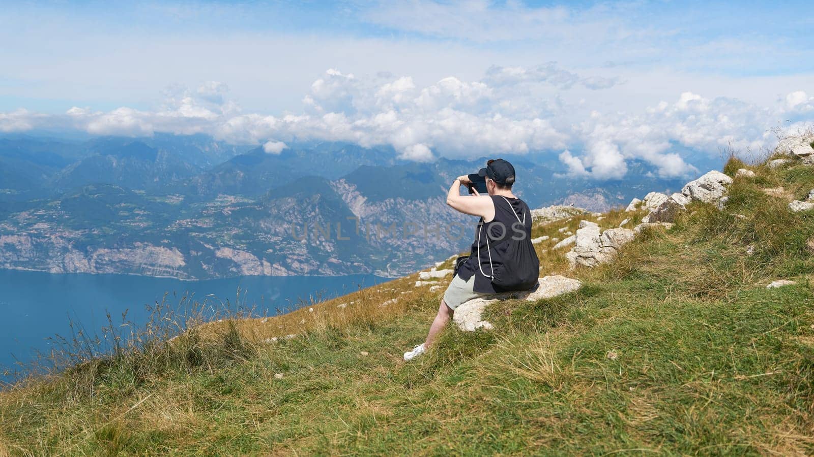 female Holidaymaker on the top of Monte Baldo on Lake Garda takes a photo of the landscape with her smartphone